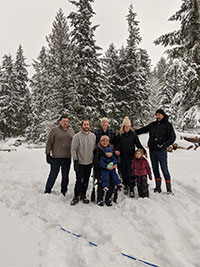 Our family photo of eight, with two grandchildren, our sons and daughter and us the grandparents, taken in a snowy bench pasture.