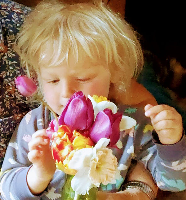 young blond two year old child admiring a spring bouquet.